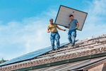 2 Arbeiter tragen ein PV-Modul über ein Hausdach
