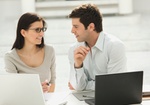 Mann und Frau sitzen an Laptops, unterhalten sich