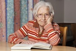 Seniorin liest ein Buch und schaut in die Kamera